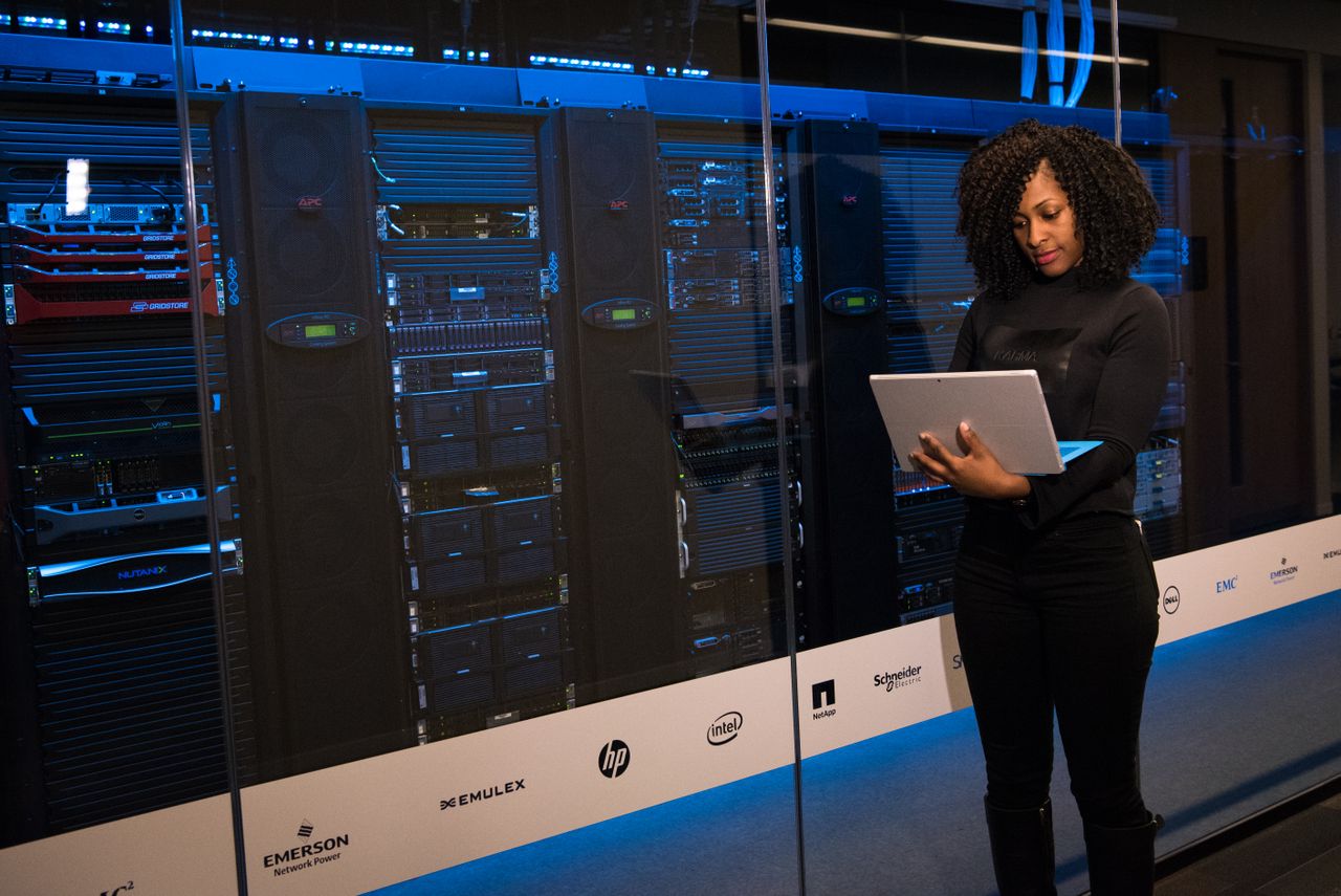 about-img A female engineer using a laptop while monitoring data servers in a modern server room.